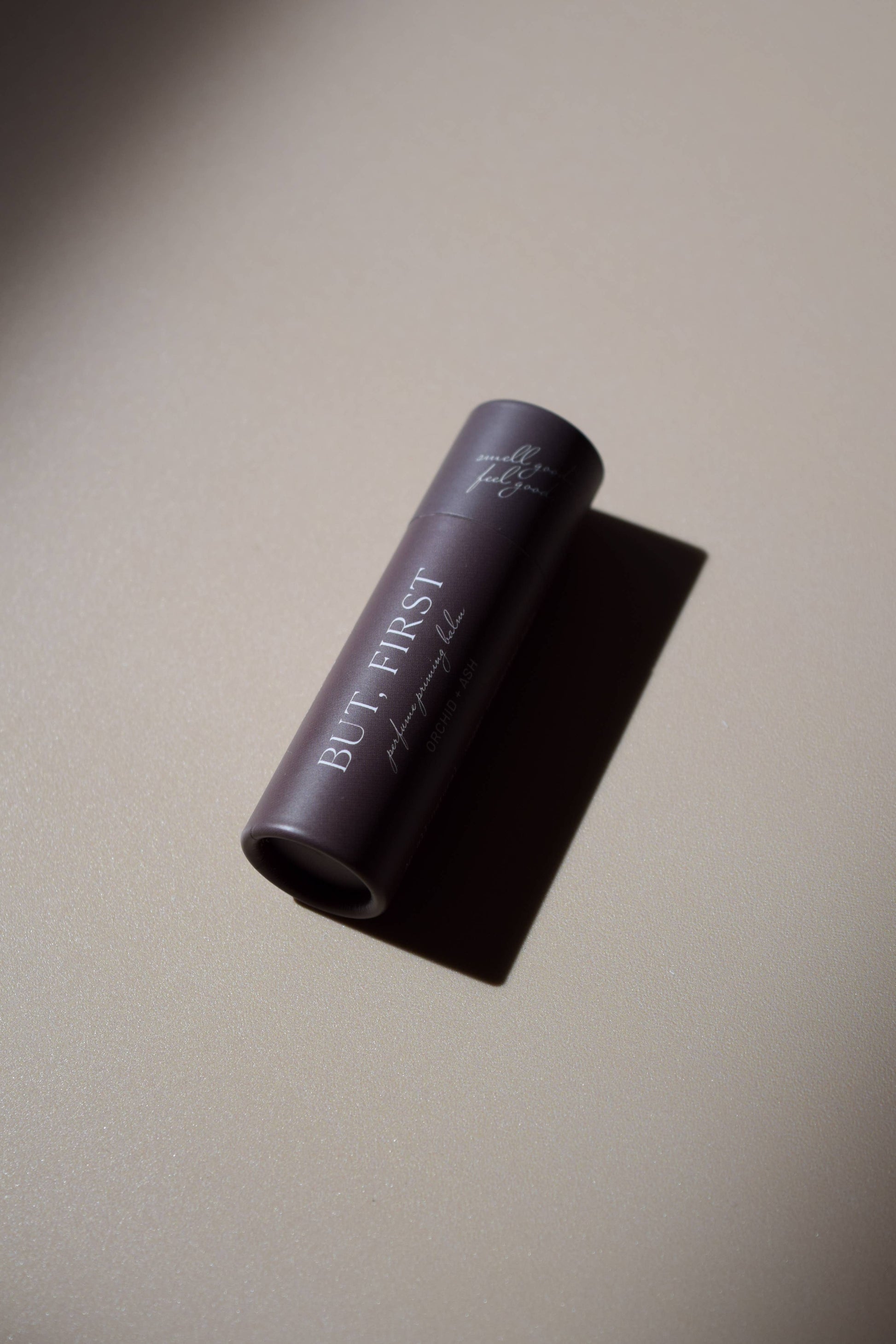 But First natural perfume balm by Orchid & Ash laying flat, casting a dramatic shadow on a matte surface.