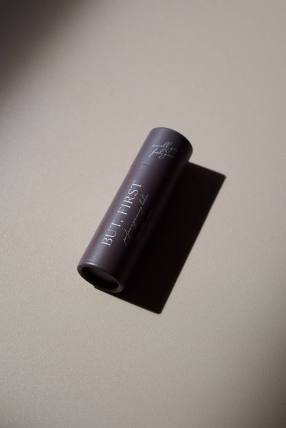 But First natural perfume balm by Orchid & Ash laying flat, casting a dramatic shadow on a matte surface.
