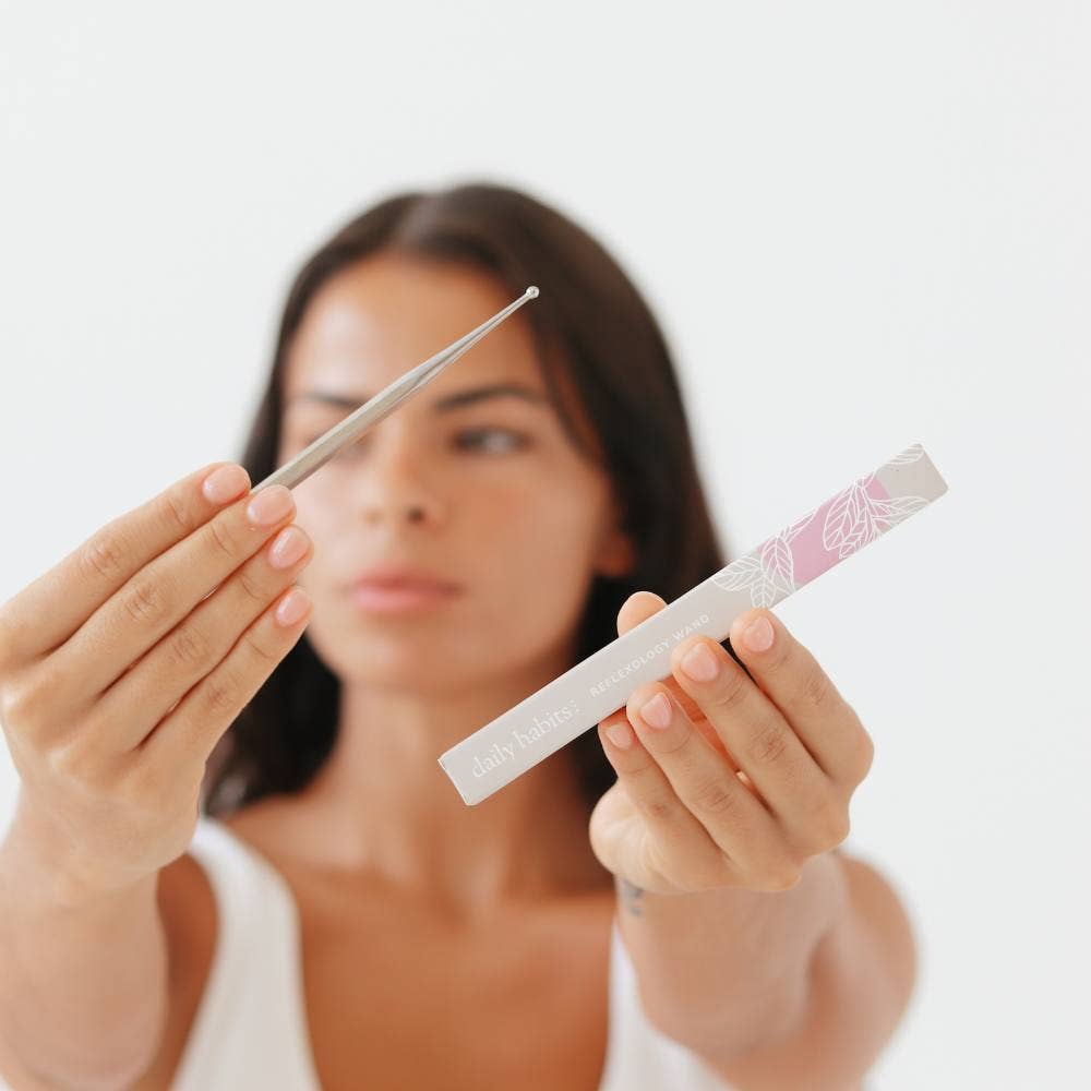 Woman holding Daily Habits Facial Reflexology Tool with pink and grey packaging.