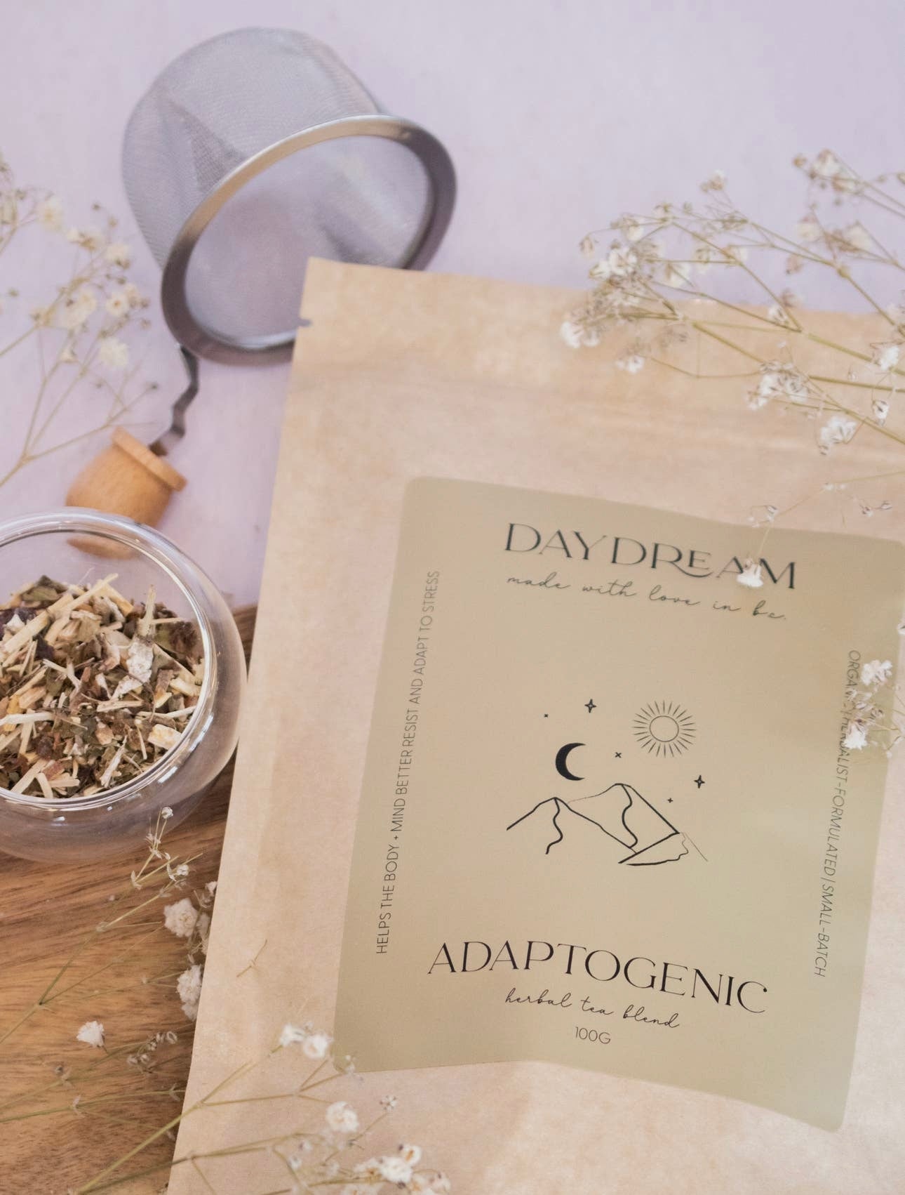 Flat lay of Daydream Organics Adaptogenic Herbal Tea pouch surrounded by a tea infuser and dried flowers.