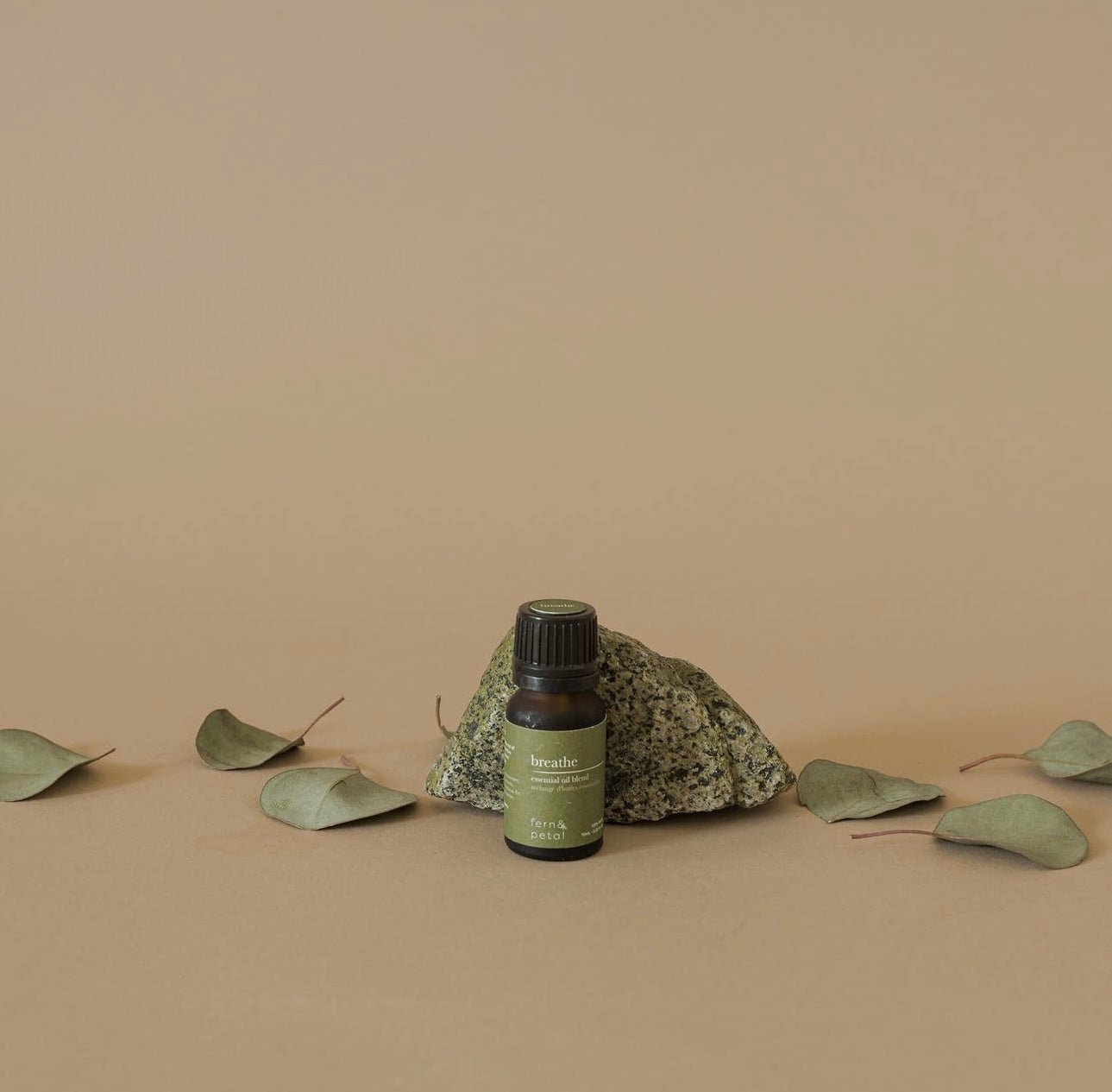 Fern & Petal Breathe Essential Oil Blend bottle placed beside eucalyptus leaves and a stone on a neutral background.