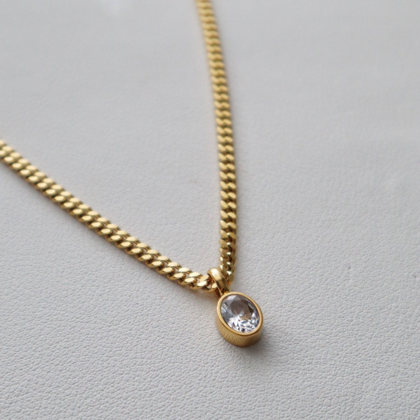 Close-up of JESSA Jewelry gold chain necklace with oval CZ gem pendant on textured surface.