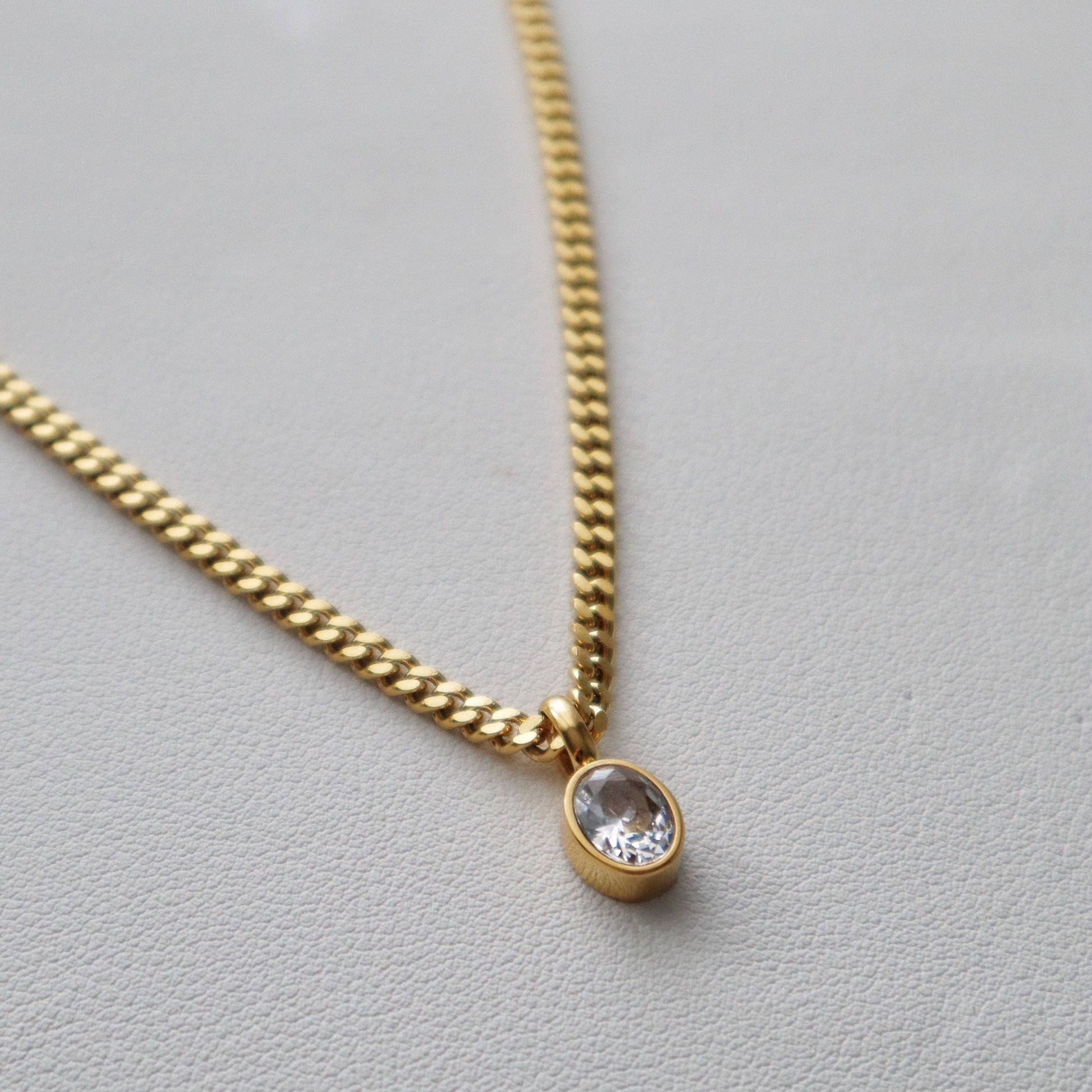 Close-up of JESSA Jewelry gold chain necklace with oval CZ gem pendant on textured surface.