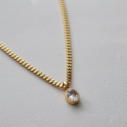 Close-up of JESSA Jewelry gold chain necklace with oval CZ gem pendant on textured surface.