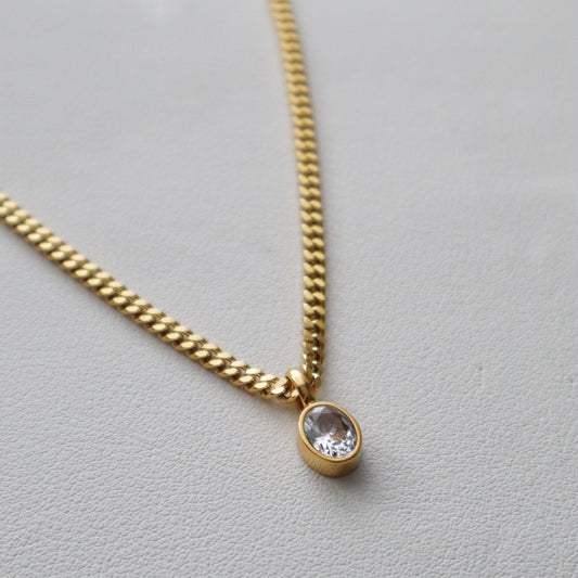 Close-up of JESSA Jewelry gold chain necklace with oval CZ gem pendant on textured surface.