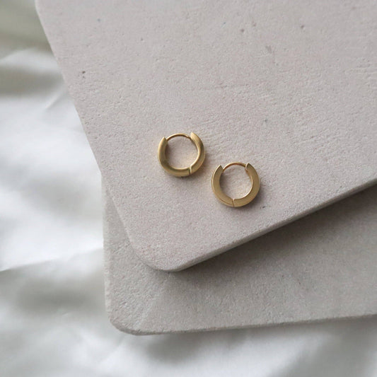 Flatlay of gold Sadie hoops by JESSA Jewelry on soft neutral-toned fabric and suede backdrops.