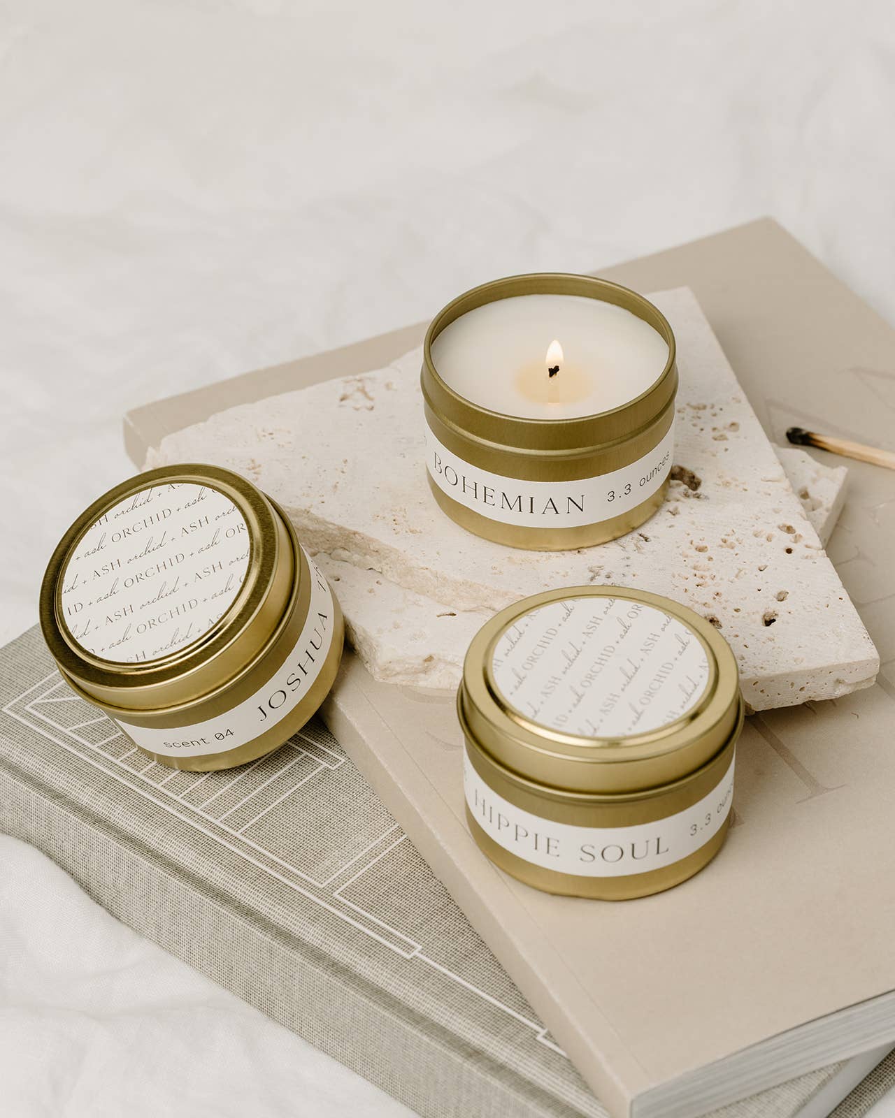 Tins of Bohemian, Hippie Soul, and Joshua Tree candles by Orchid & Ash displayed on stacked books and stone.