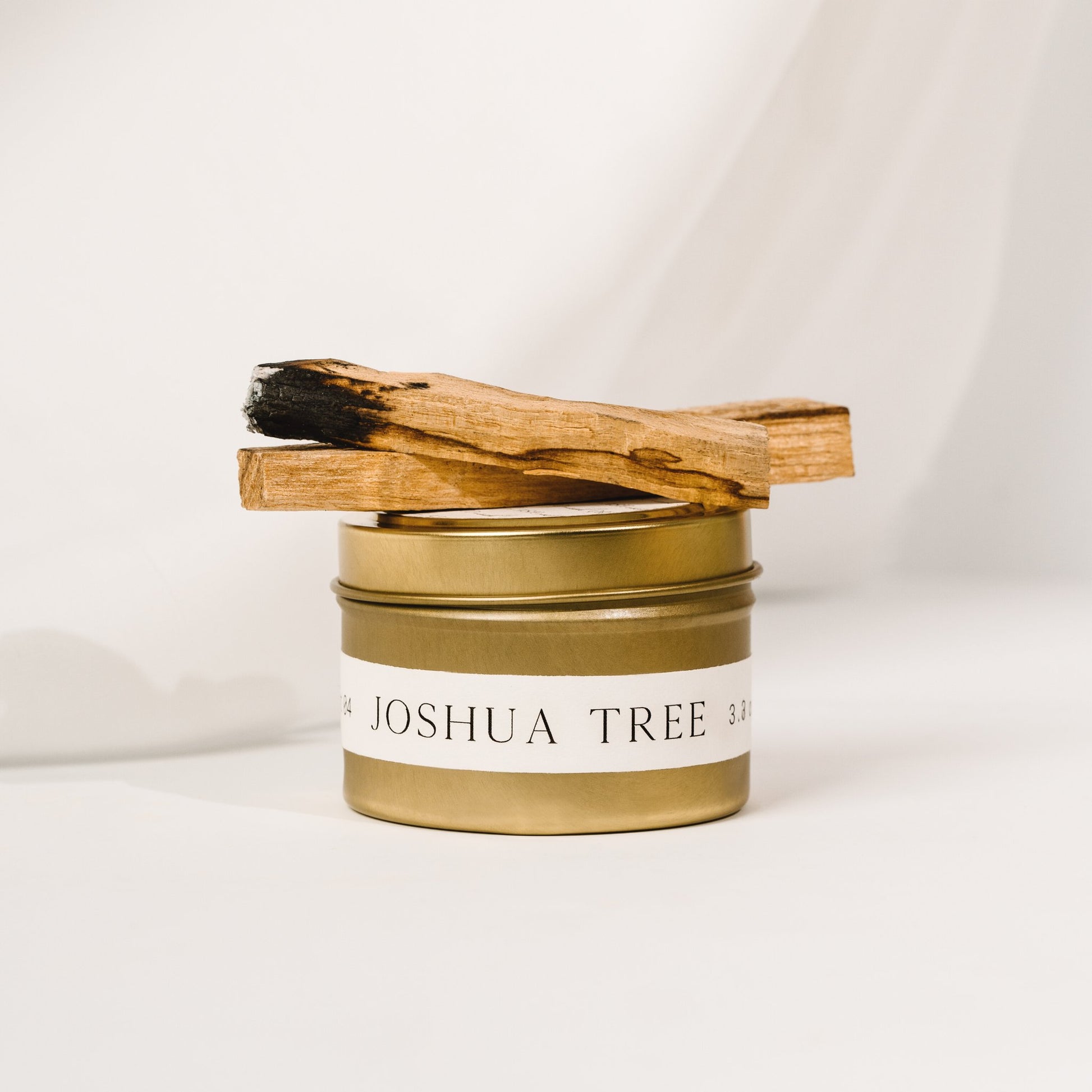 Joshua Tree gold candle tin by Orchid & Ash styled with palo santo and white soft background.