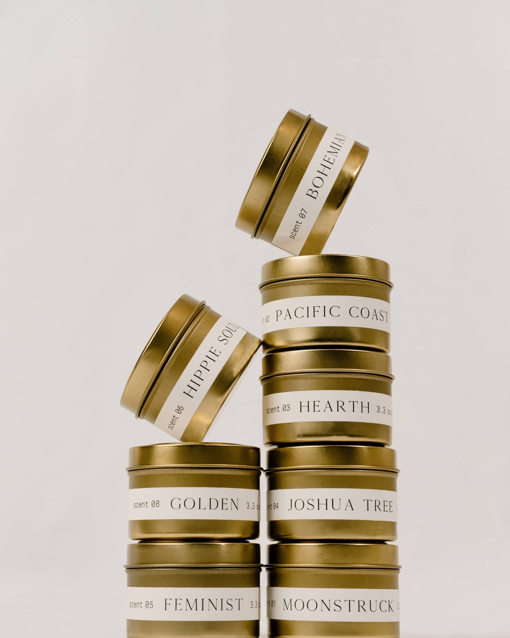 Stack of Orchid & Ash tin candles featuring Hippie Soul, Golden, Feminist, Moonstruck, Joshua Tree, Hearth, Pacific Coast and Bohemian.