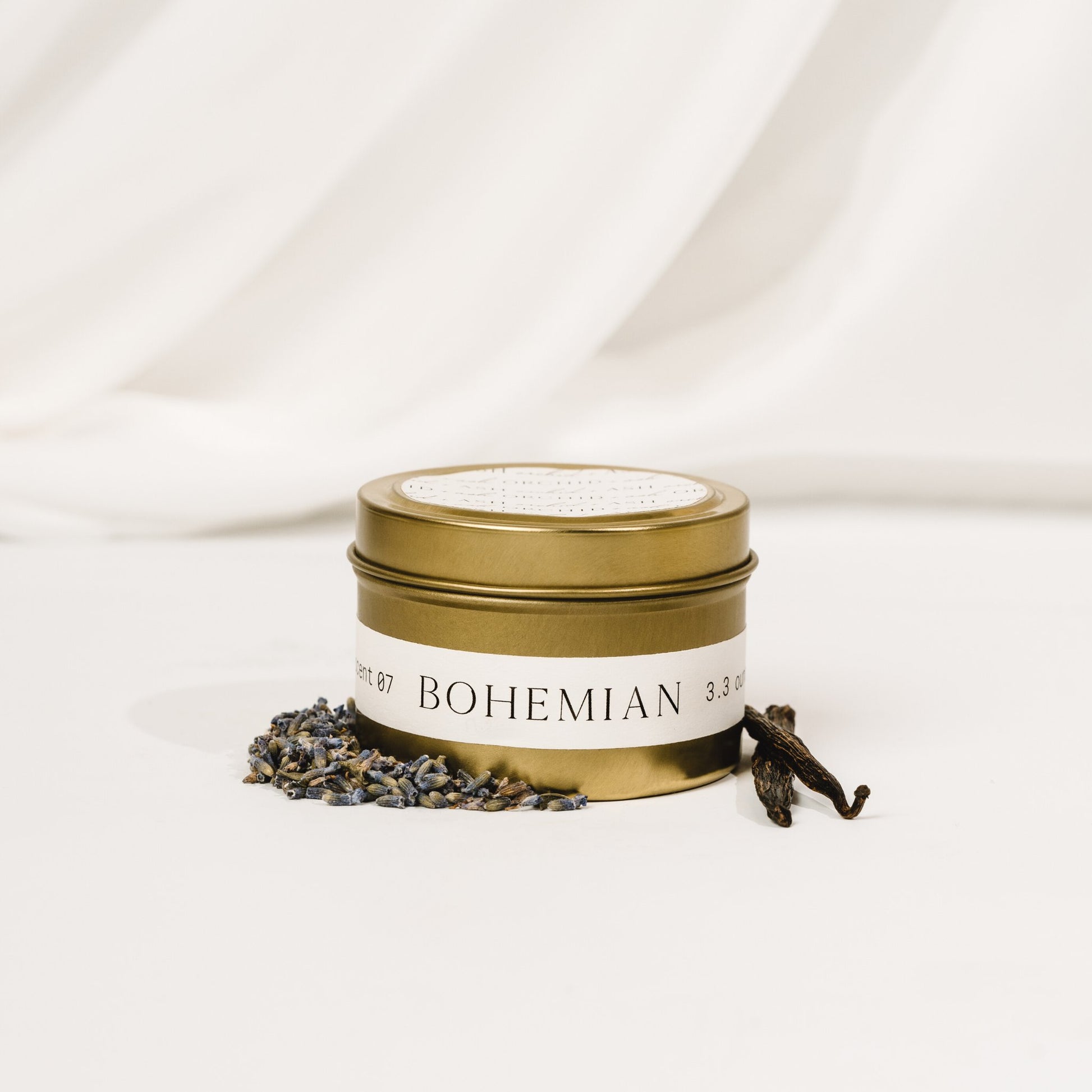 Orchid & Ash Bohemian scented candle in a gold tin surrounded by lavender and vanilla pods.
