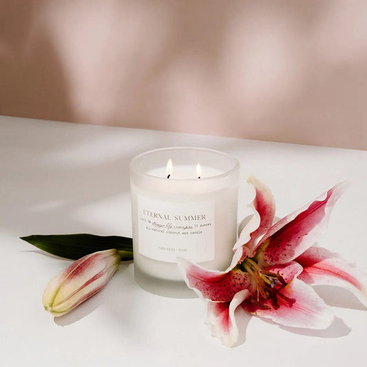 Eternal Summer candle by Orchid & Ash styled with open lilies on a white surface with soft shadows.