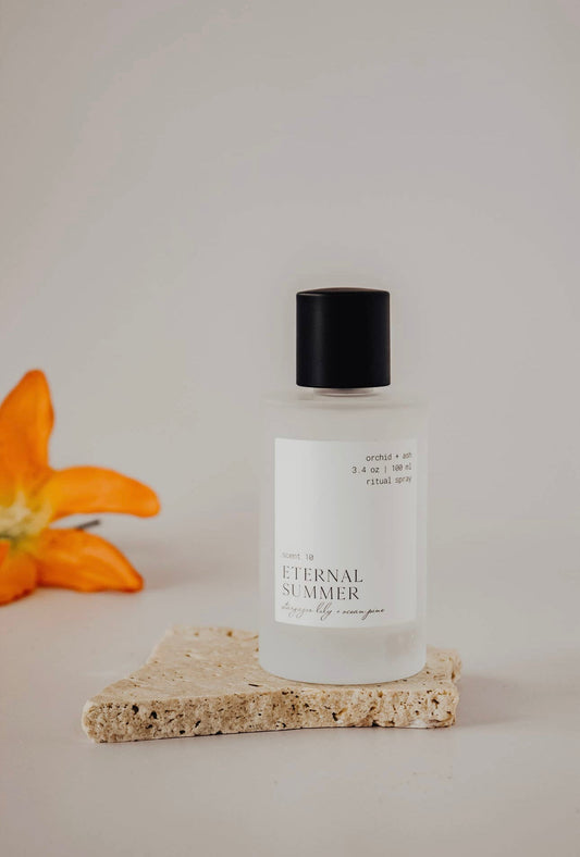 Eternal Summer room spray by Orchid & Ash displayed on natural stone with an orange lily.