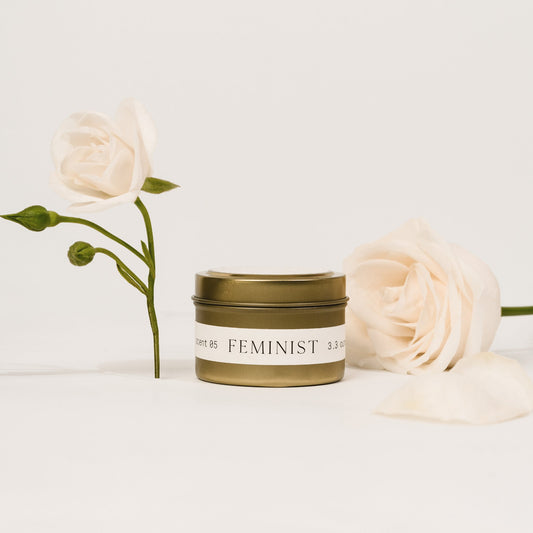 Orchid & Ash Feminist candle in a gold tin styled with soft ivory rose florals.