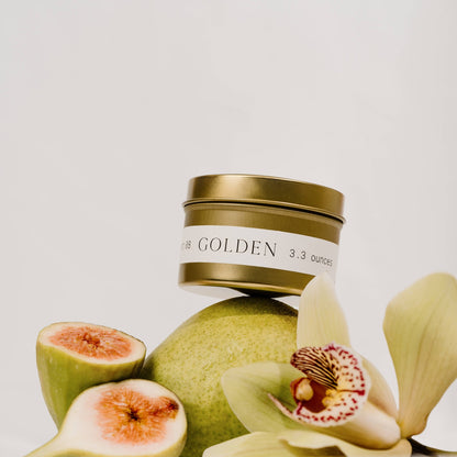 Golden tin candle by Orchid & Ash displayed with an orchid bloom, fig, and pear.