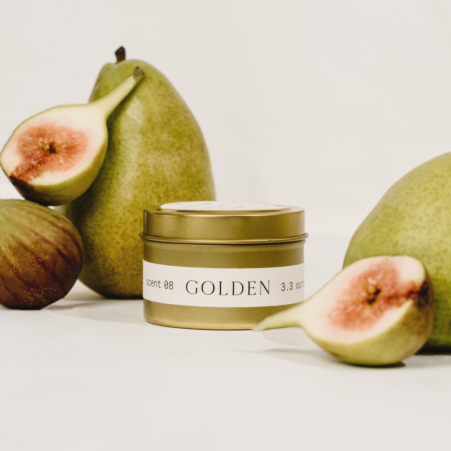 Orchid & Ash Golden tin candle surrounded by pears and figs on a soft white backdrop.