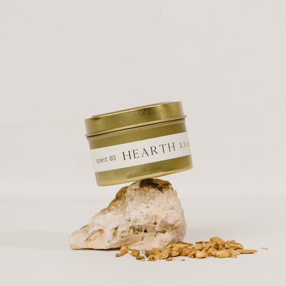 Hearth tin candle by Orchid & Ash balanced atop a rock with granules, minimalist studio backdrop.