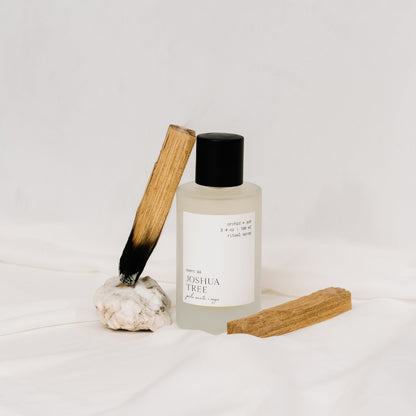 Orchid & Ash Joshua Tree room spray styled with palo santo and crystals on white fabric.