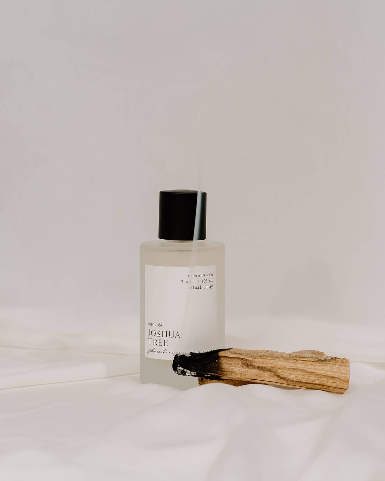 Minimal styling of Orchid & Ash Joshua Tree room spray bottle with black top and burning palo santo on soft white backdrop.