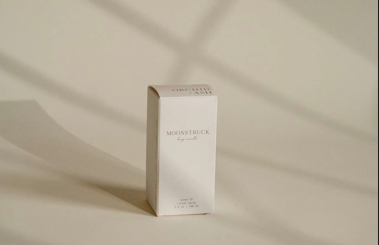 Minimalist packaging of Orchid & Ash room linen spray bathed in soft shadowed light.