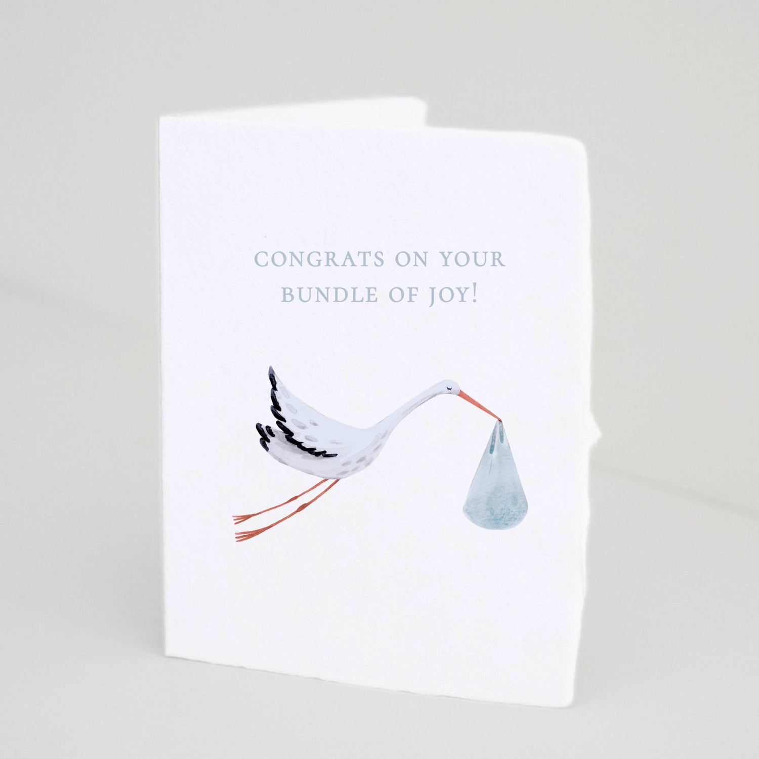 Front of Paper Baristas baby boy greeting card with illustrated stork carrying a blue bundle and text that reads “Congrats on your Bundle of Joy!”