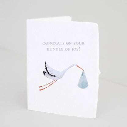 Front of Paper Baristas baby boy greeting card with illustrated stork carrying a blue bundle and text that reads “Congrats on your Bundle of Joy!”