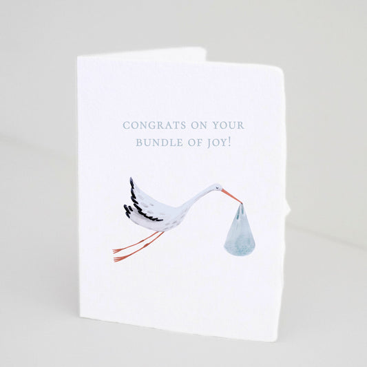Front of Paper Baristas baby boy greeting card with illustrated stork carrying a blue bundle and text that reads “Congrats on your Bundle of Joy!”