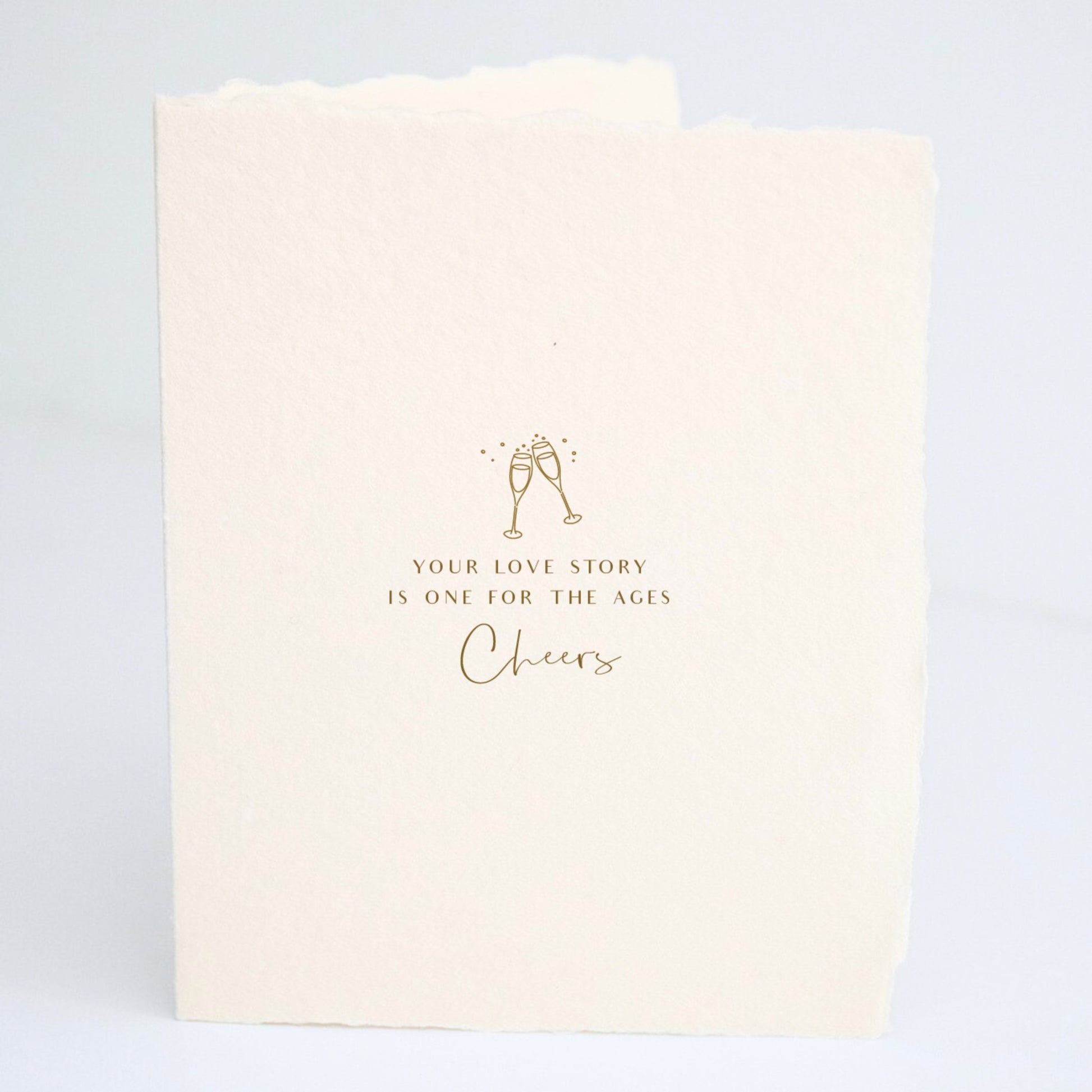 Front of Paper Baristas wedding card with champagne glasses illustration and the words “Your love story is one for the ages. Cheers" in gold foil.