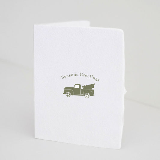 Front of Paper Baristas holiday card with vintage truck carrying a tree and “Seasons Greetings” text.