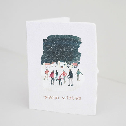 Front of Paper Baristas holiday card featuring an ice skating scene with “warm wishes” in gold foil.