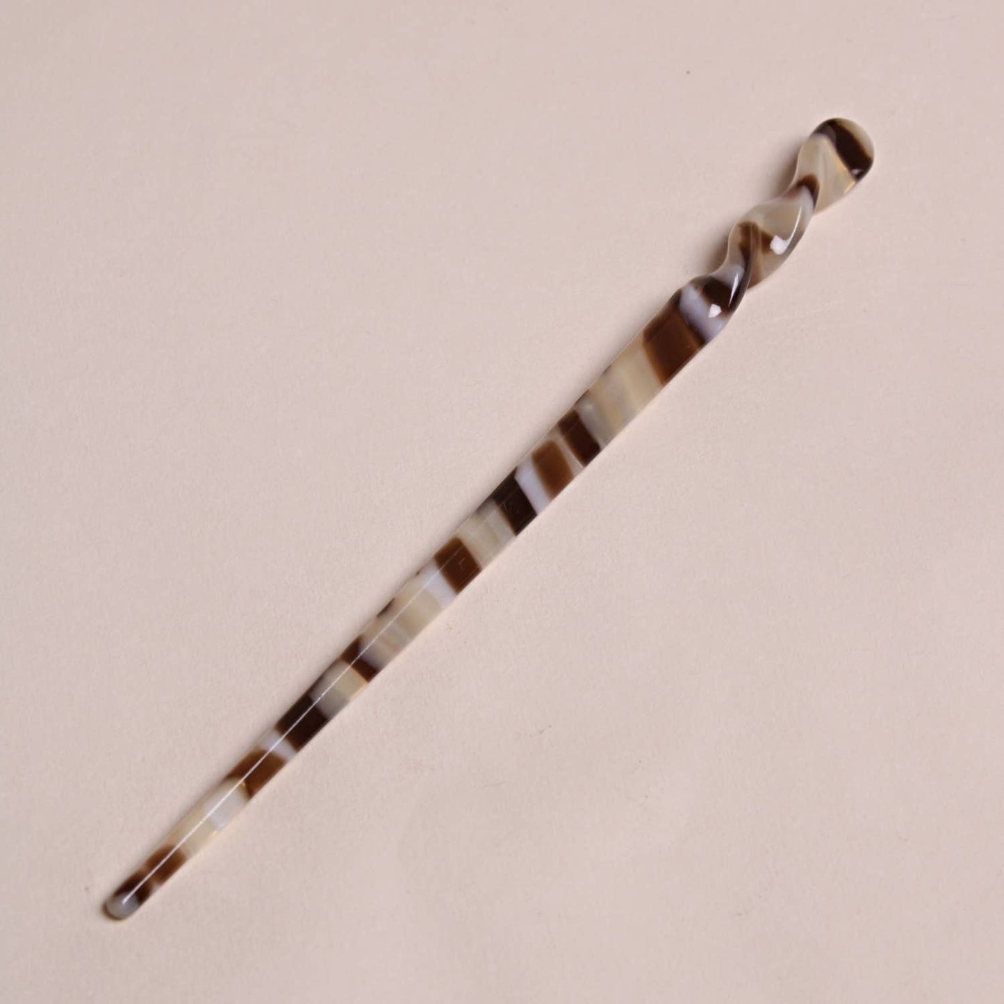 Mocha-colored Peignée Paris acetate hair stick pin with dark and light brown swirls on a flat background.