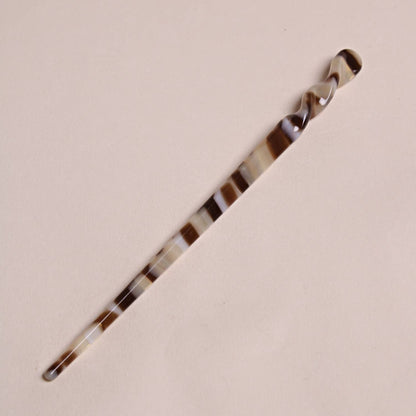 Mocha-colored Peignée Paris acetate hair stick pin with dark and light brown swirls on a flat background.