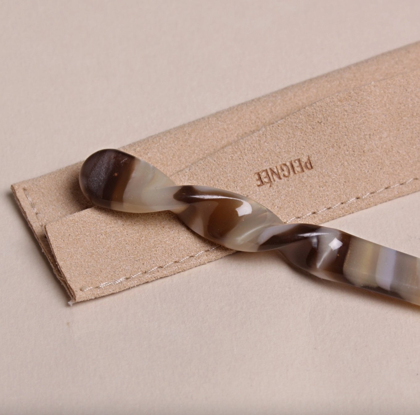 Mocha Peignée Paris hair stick pin displayed next to protective suede case with logo embossing.