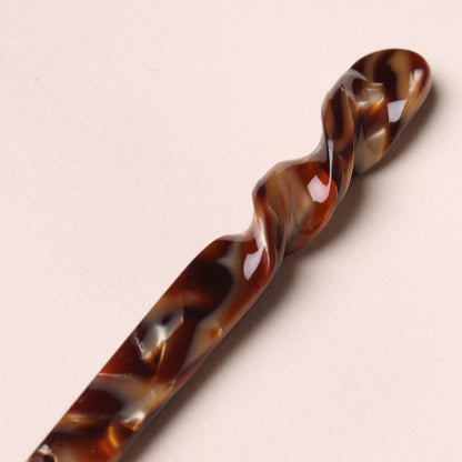 Close-up of the twisted details of the espresso colored Peignée Paris hair stick pin on neutral background.