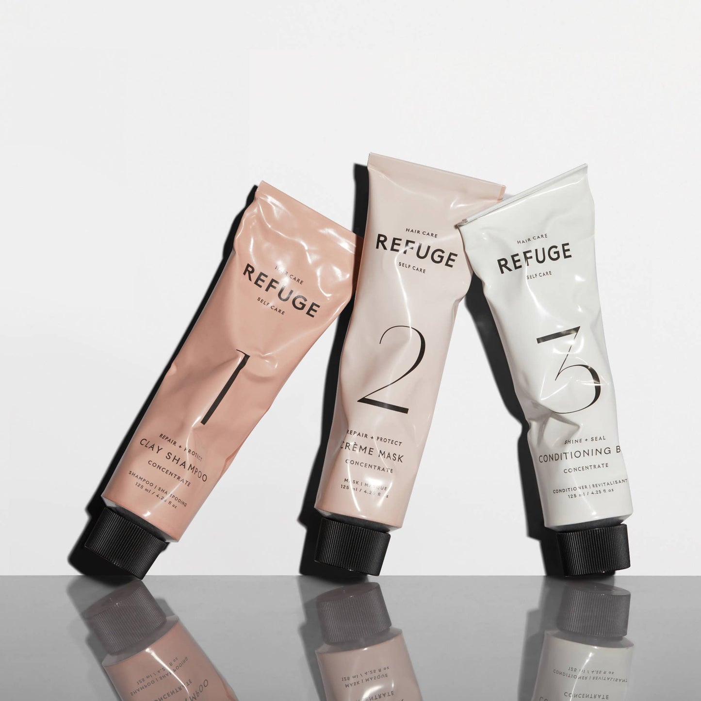 Trio of REFUGE Hair Care products angled on a reflective surface, emphasizing their sleek packaging design - Wellaine