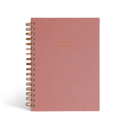 The Self Care Planner Weekly Edition in dusty rose color, front cover with gold foil text.