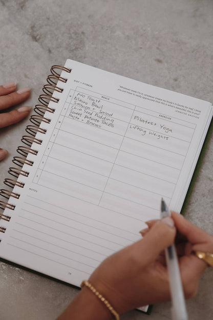 Close-up of someone writing in The Self Care Planner weekly spread, filling in schedule and exercise goals.