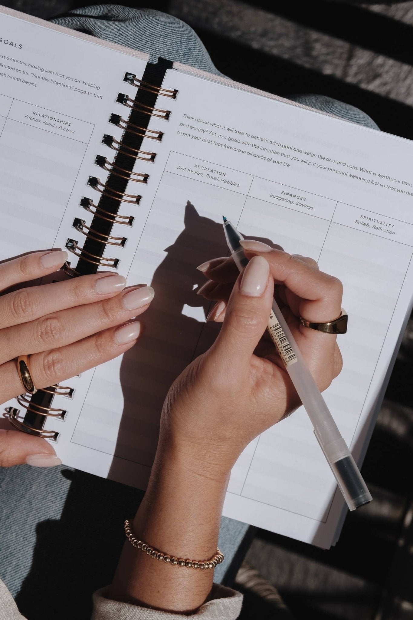 Hands holding The Self Care Planner while writing focus goals for recreations, finances, and spirituality.