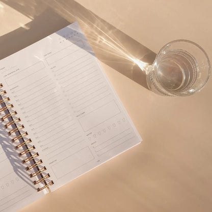 The Self Care Planner open to a blank weekly planning page with a glass of water casting shine and shadows.
