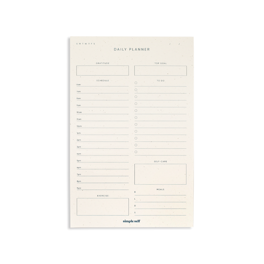 Flatlay of Simple Self Daily Planner Notepad showing sections for gratitude, top goal, schedule, to-do list, exercise, meals, and self-care.

