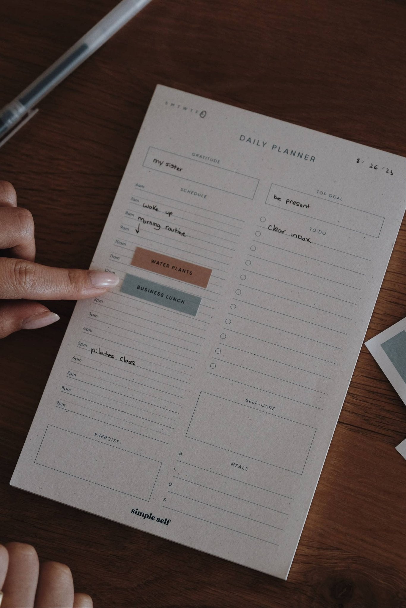 Close-up of a Simple Self Co Work Sticker being applied to a daily planner on a wooden desk.