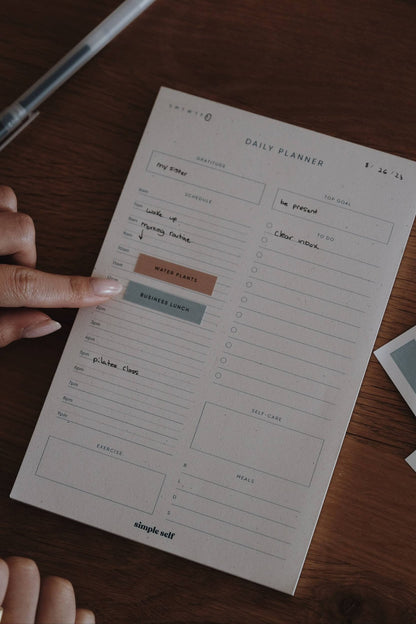 Close-up of a Simple Self Co Work Sticker being applied to a daily planner on a wooden desk.