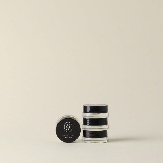 Three stacked jars of Sunday Standard Hydrating Lip Butter Salve with one jar on side, showcasing minimalist black and clear packaging.
