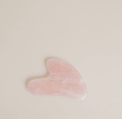 A pink colored Rose Quartz Gua Sha facial massage tool on a light neutral background.