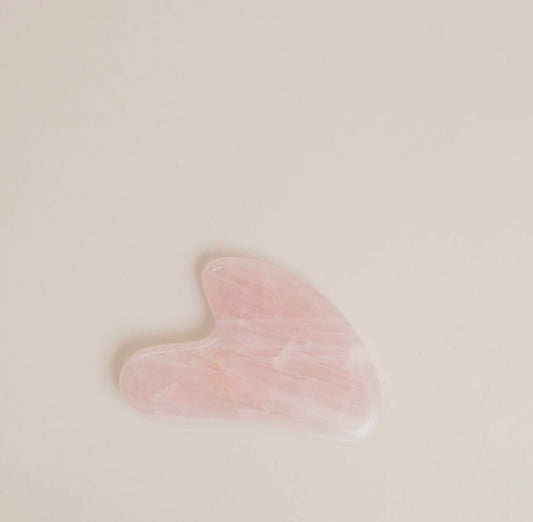 A pink colored Rose Quartz Gua Sha facial massage tool on a light neutral background.
