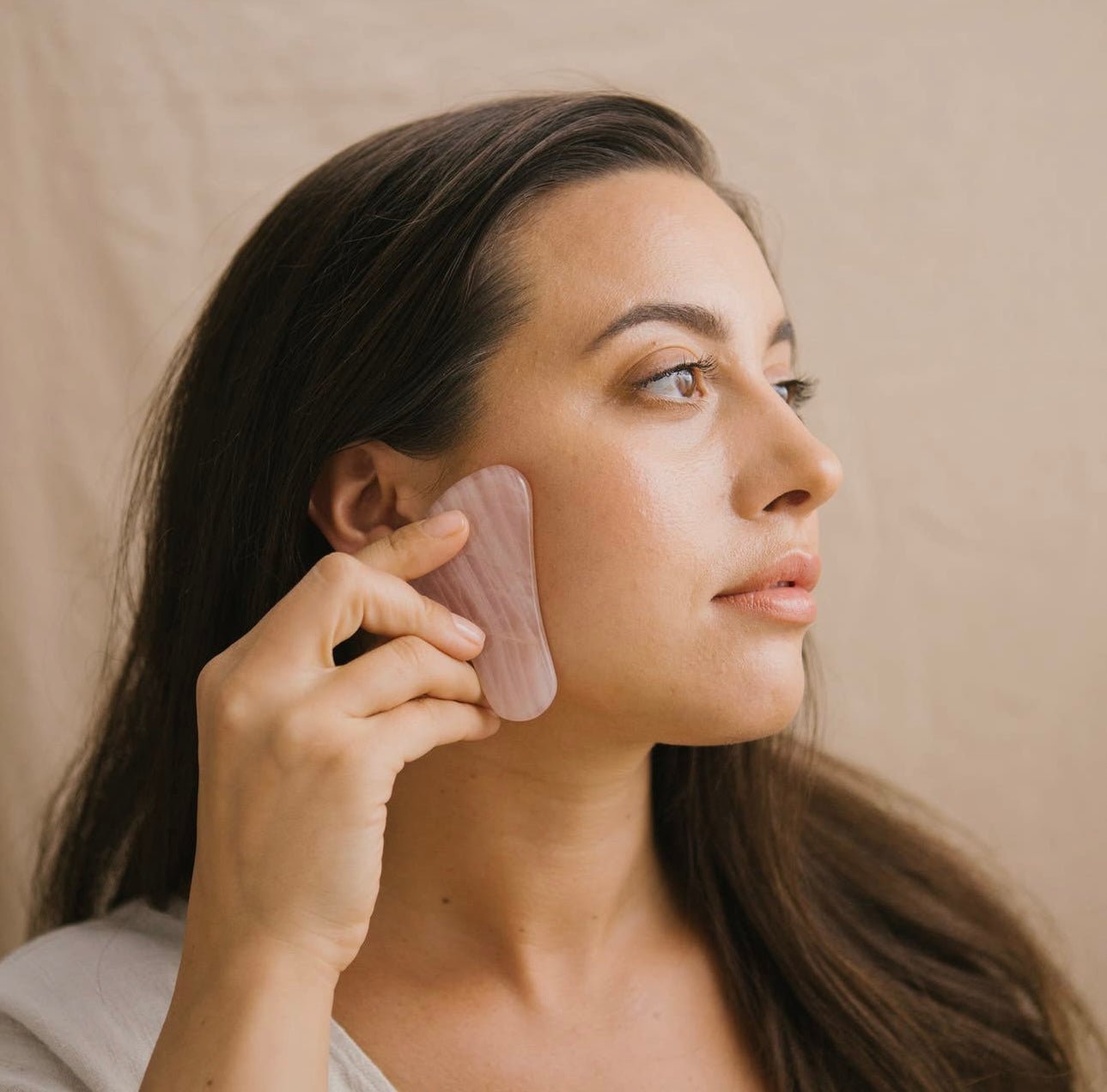 Woman lifting her cheek area with the flat side of Rose Quartz Gua Sha facial tool.
