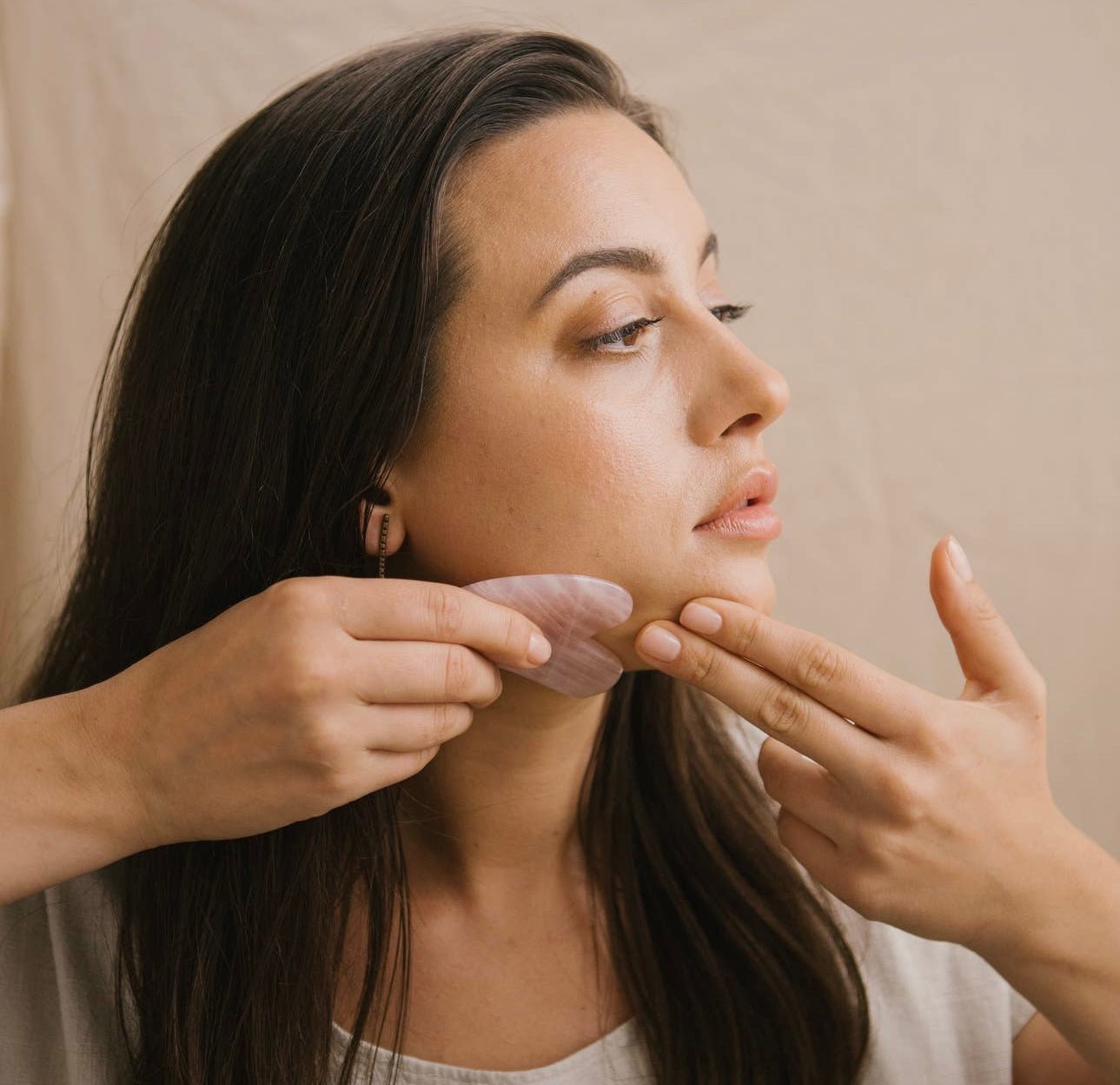 Close-up of a woman using the Rose Quartz Gua Sha facial tool along the jawline.