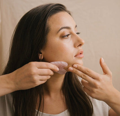 Close-up of a woman using the Rose Quartz Gua Sha facial tool along the jawline.
