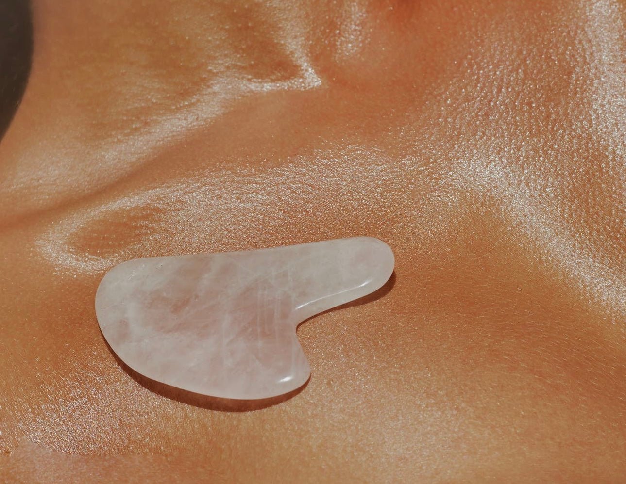 Close-up of a Rose Quartz Gua Sha tool resting on smooth, glowing skin.