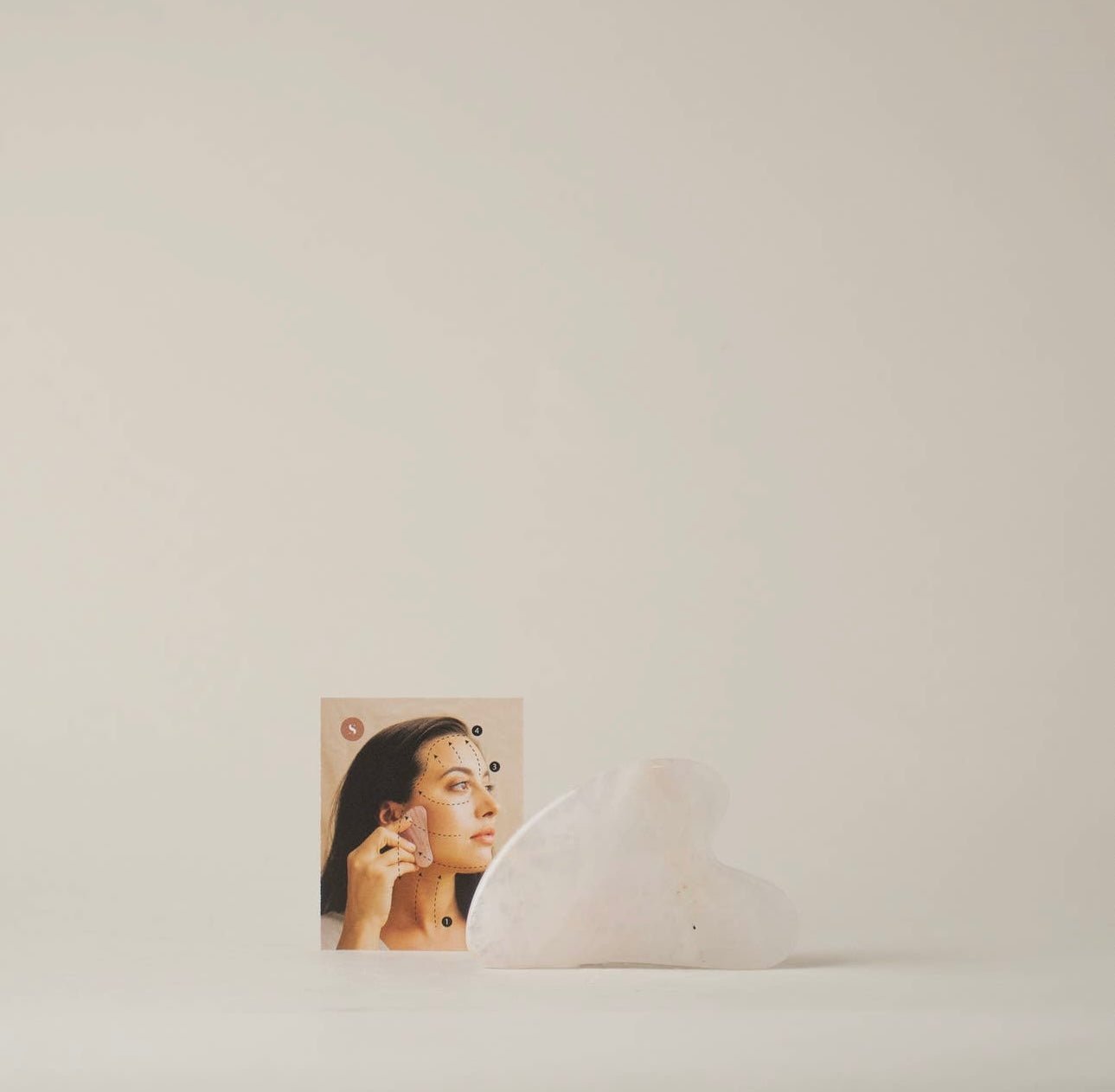 Rose Quartz Gua Sha tool displayed next to its packaging with an instruction card with image of a model using product.
