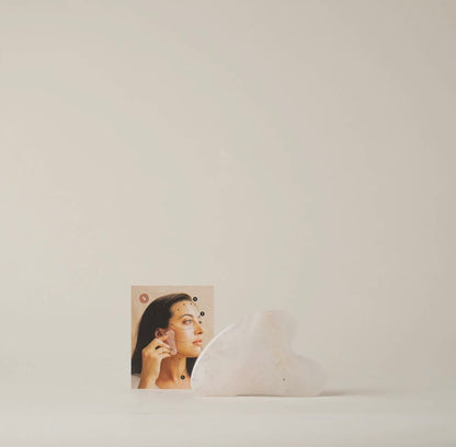Rose Quartz Gua Sha tool displayed next to its packaging with an instruction card with image of a model using product.
